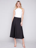 Jupe en satin noir pour femme, taille élastique, 97% polyester, 3% spandex. Vue complète de la jupe portée avec des talons transparents.